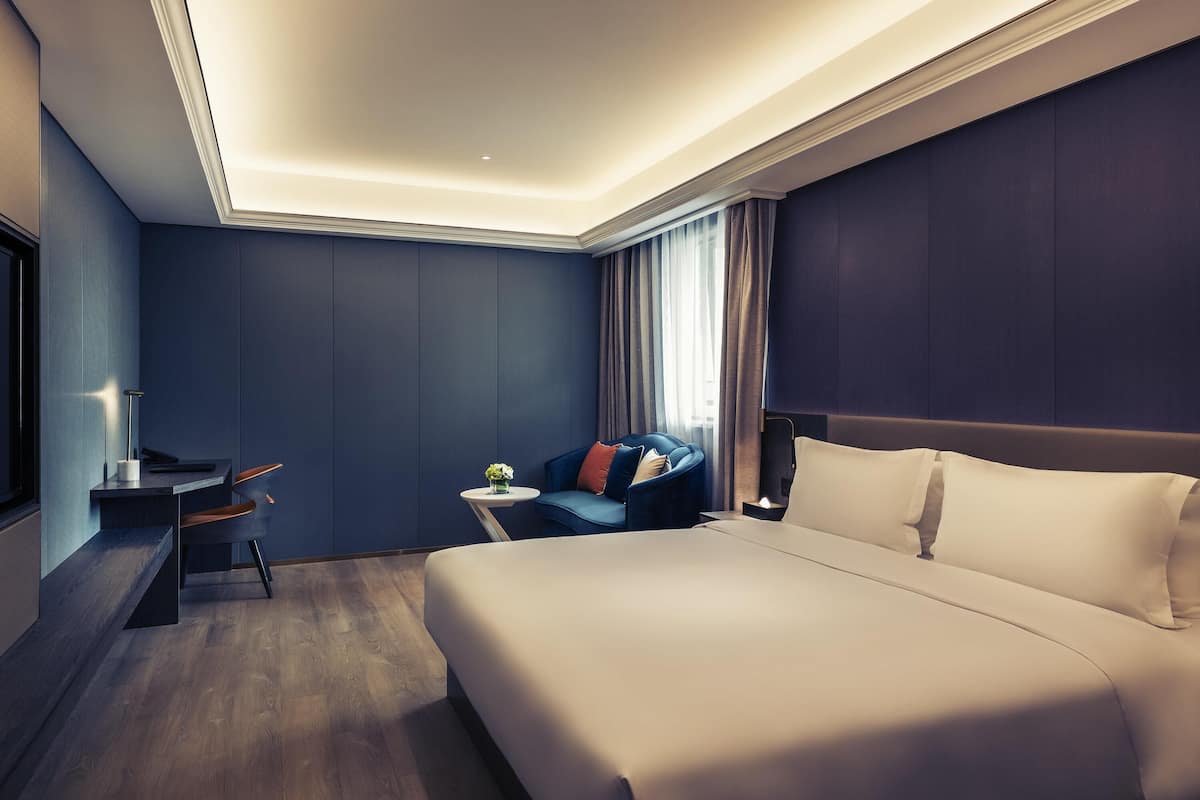Una habitación de hotel moderna con una cama grande, un escritorio, una silla y una mesita con un jarrón de flores.
