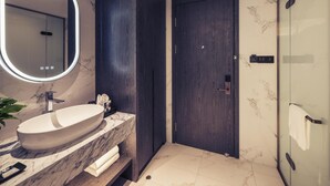 A modern bathroom with a large oval sink, a dark wooden door, and a glass shower enclosure.