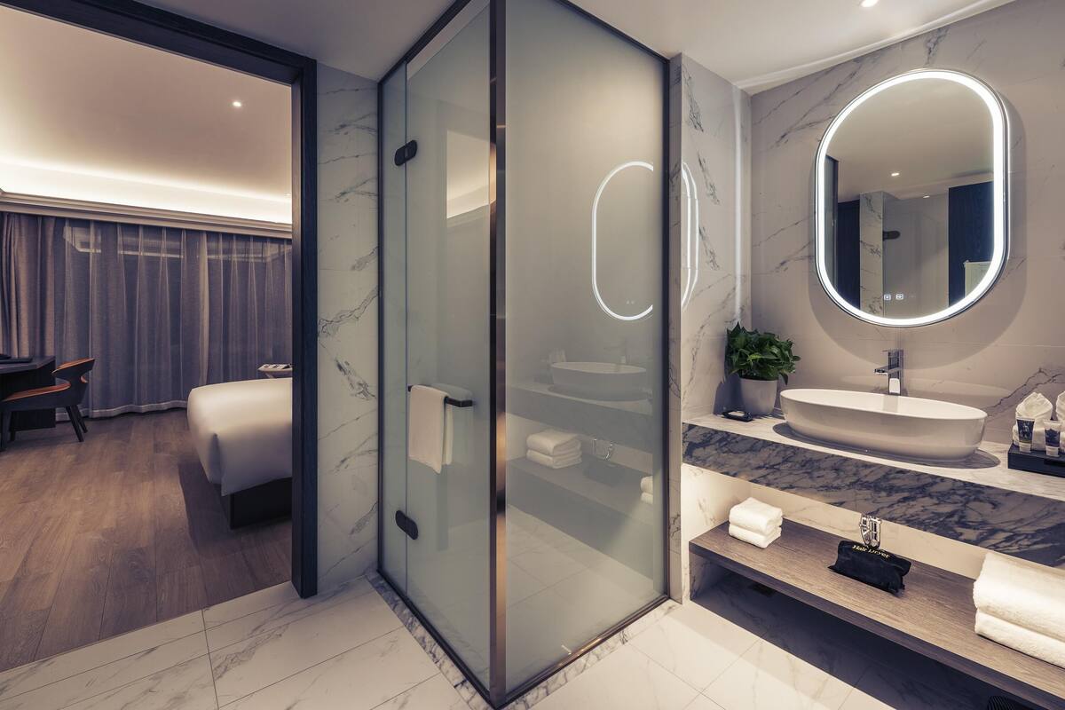 Un baño moderno con ducha envuelta en vidrio, tocador con azulejos de mármol y un espejo grande con iluminación integrada.