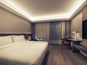 Una habitación de hotel con una cama grande, un escritorio, una silla, una mesita con una planta y un televisor en la pared.