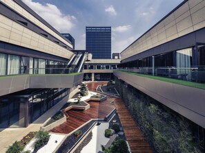 Un edifici modern amb un atrium central, baranes de vidre i un jardí al terrat.