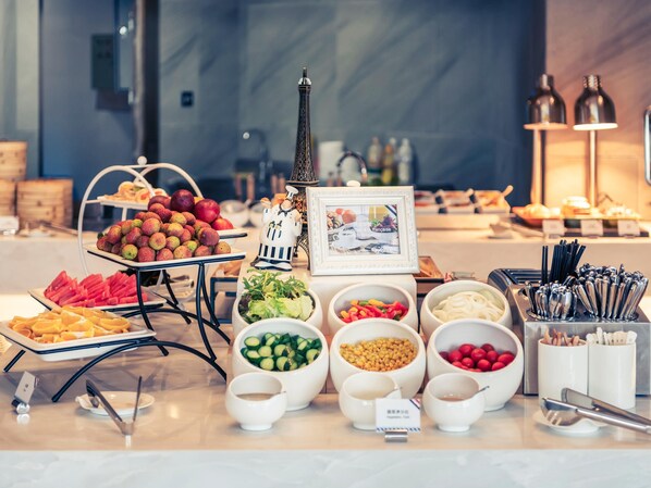 A buffet with various food items, including fruits, vegetables, and condiments, arranged on a table with a decorative Eiffel Tower and a framed picture. - Mercure Shanghai Necc (Shanghai)