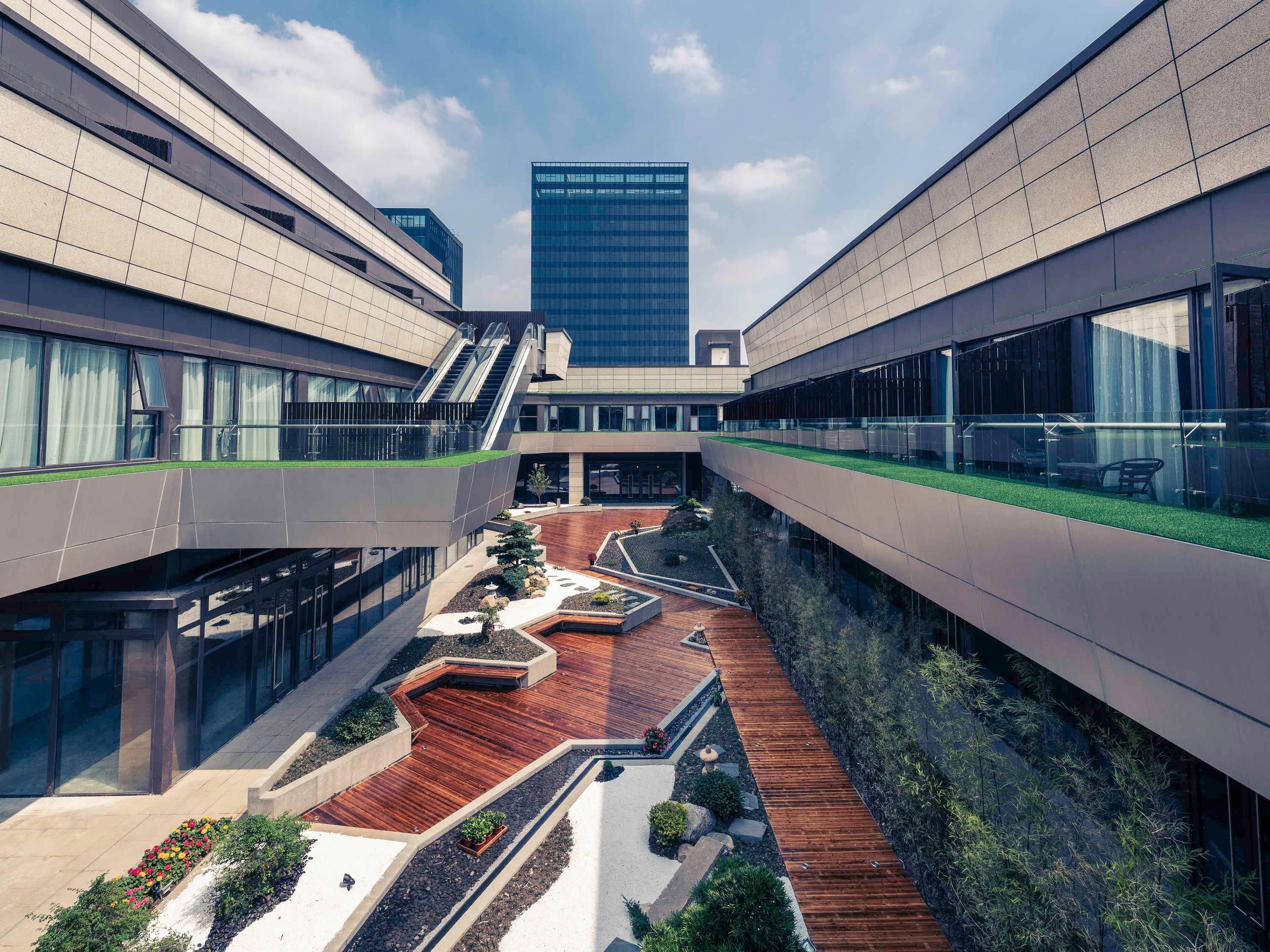 A modern building with a central courtyard, glass railings, and a view of a tall skyscraper.
