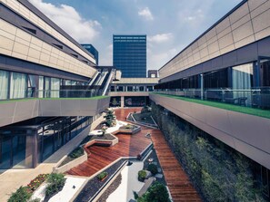 Un edificio moderno con un patio central, barandillas de vidrio y vistas a un rascacielos alto.