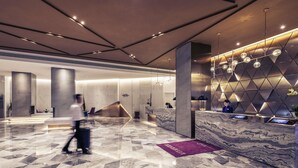 A modern hotel lobby with marble flooring, a reception desk, and a geometric wall design.