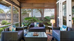 A covered patio with wicker furniture, a glass coffee table, and a view of a backyard. - Private Pool, Steps to Beach, Screen in Porch, Cutest Cottage in Crystal Beach! (Destin)