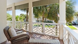 A covered porch with wicker furniture, white railings, and a view of palm trees and a street. - Close to Beach~Golf Cart! Pet Friendly Home! Pool! Destiny West (Destin)