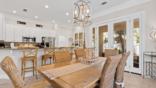A spacious kitchen with white cabinets, stainless steel appliances, and a dining area with a wooden table and wicker chairs. - Close to Beach~Golf Cart! Pet Friendly Home! Pool! Destiny West (Destin)