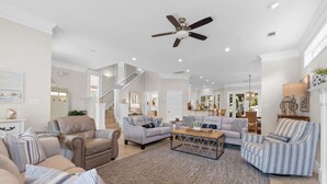 A spacious living room with a high ceiling fan, a staircase leading to an upper level, and a well-lit kitchen area. - Close to Beach~Golf Cart! Pet Friendly Home! Pool! Destiny West (Destin)