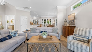 A spacious living room with a grey sofa, a patterned armchair, and a wooden coffee table. - Close to Beach~Golf Cart! Pet Friendly Home! Pool! Destiny West (Destin)