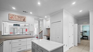 A modern kitchen with white cabinets, a large island, and a ceiling light fixture. - Steps to Beach~Private Pool~Pet Friendly~Carriage House~Optional Golf Cart! (Destin)