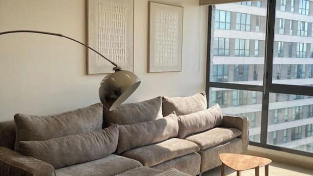 A modern living room with a grey sofa, a floor lamp, and a small wooden table. There are two framed artworks on the wall and a large window with a city view. - Polanco be grand (Ciudad de México)