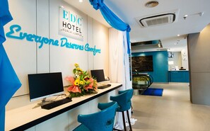 Een receptiebalie met een computer, een bloemstuk en een bord met de tekst 'EDC HOTEL KUALA LUMPUR'.