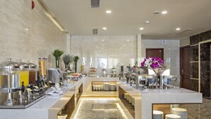Zona de l'esmorzar d'un hotel modern amb sòl de marbre, un sistema de buffet i diverses màquines de menjar i beguda.