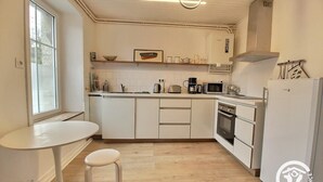 Een kleine keuken met witte kastjes, een magnetron, een koffiezetapparaat en een koelkast.
