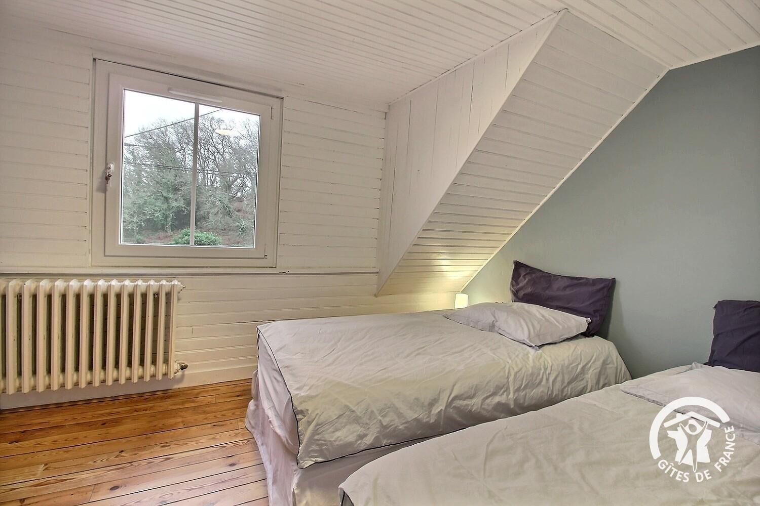 Ein Schlafzimmer mit zwei Betten, einem Fenster, einem Heizkörper und einer schrägen Decke.