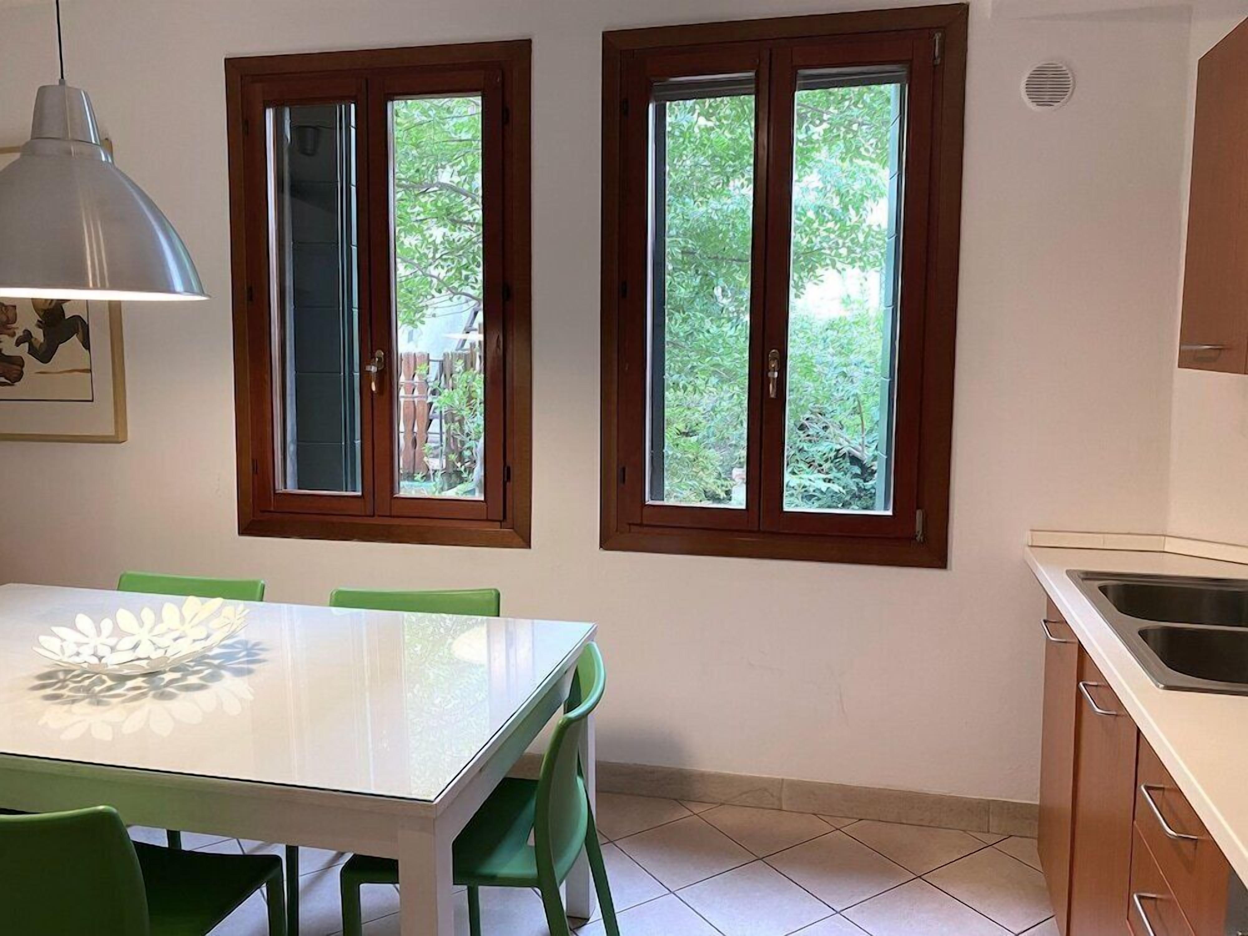 A kitchen with two windows, a dining table with chairs, and a pendant light.