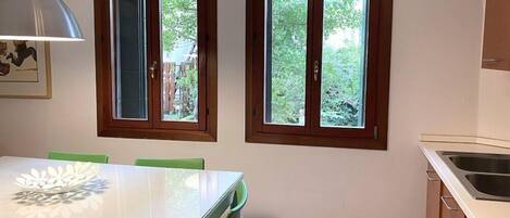 A kitchen with two windows, a dining table with chairs, and a pendant light.