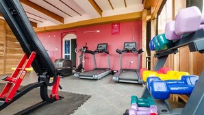 Een fitnessruimte met loopbanden, een rode trainingsmachine en gekleurde gewichten.