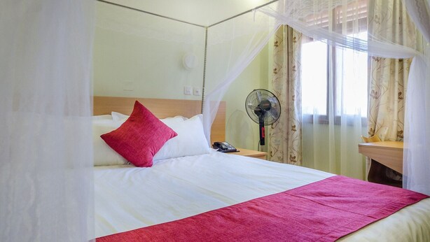 Een bed met hemel, een ventilator naast het bed en een telefoon op het nachtkastje.