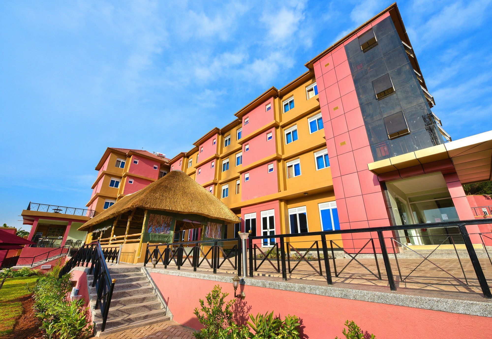 A multi-story hotel with a red and yellow facade, a thatched-roof structure, and a staircase leading to the entrance.