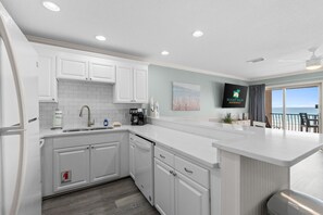 A modern kitchen with white cabinetry, a built-in island, and a view of the ocean through a large window. - NEW! Stunning Gulf-Front Condo w/ Balcony Views | Beach Service | Crystal Beach (Destin)