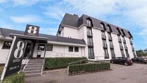 A hotel with a modern design, featuring a prominent '8' logo, a staircase leading to the entrance, and a parking area with cars. - Tulip Inn Bodegraven (Bodegraven)
