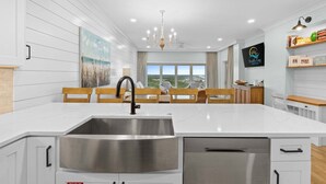 A modern kitchen with a large island, stainless steel sink, and wooden chairs. - New! Beach Manor 1005 Gorgeous Remodeled Condo w/ Gulf Views & Resort Amenities (Miramar Beach)