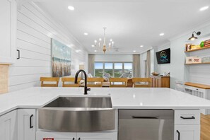 A modern kitchen with a large island, stainless steel sink, and wooden chairs. - New! Beach Manor 1005 Gorgeous Remodeled Condo w/ Gulf Views & Resort Amenities (Miramar Beach)