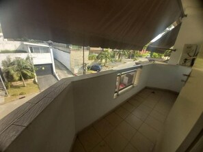 Ein Balkon mit Blick auf eine Wohngegend, darunter ein parkendes Auto und ein Gebäude mit weißer Fassade.