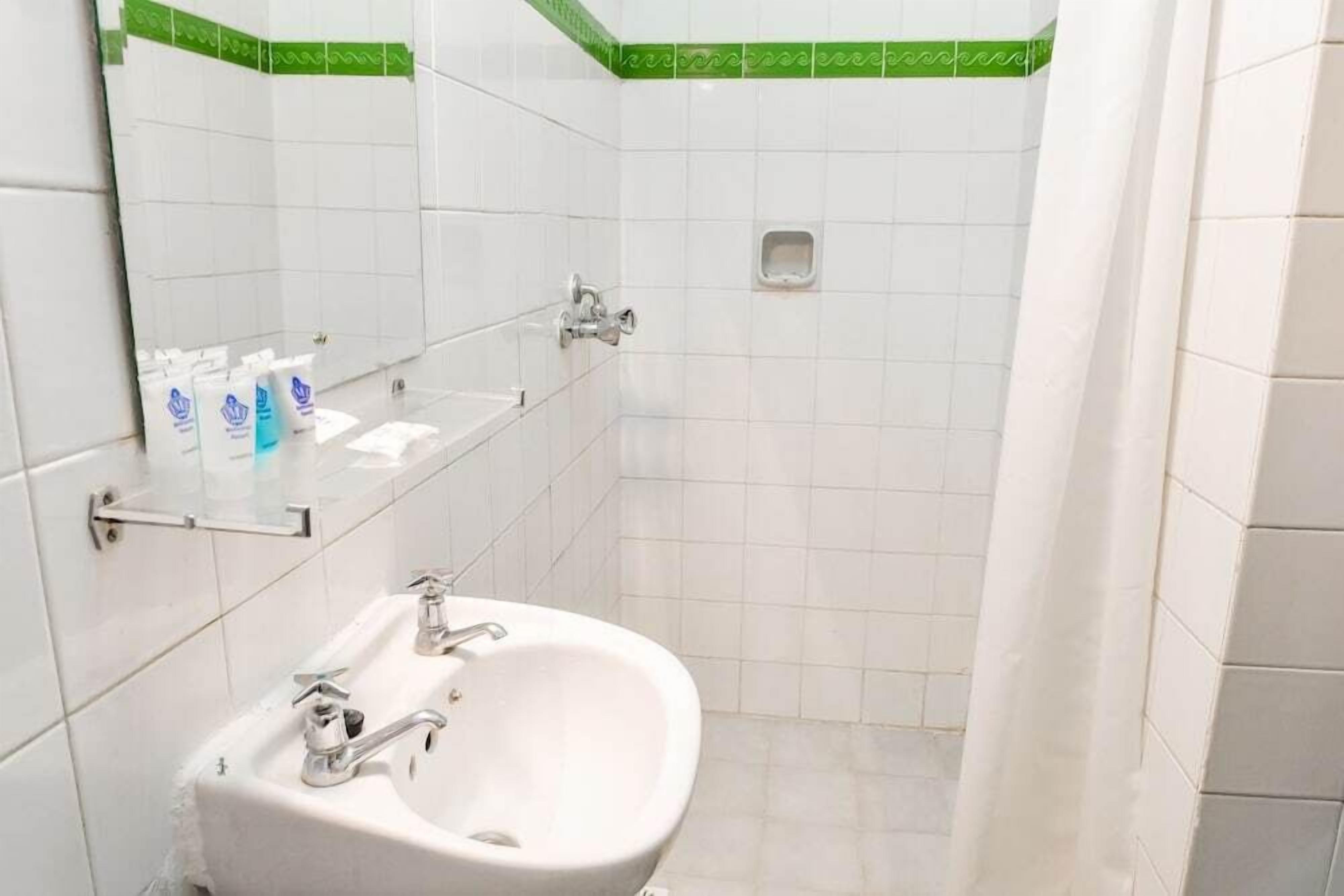A bathroom with a white sink, mirror, and green-tiled shower area.