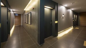 A modern hallway with a dark floor, recessed lighting, and a wooden accent wall. - Guseo Station Brown Dot (Busan)