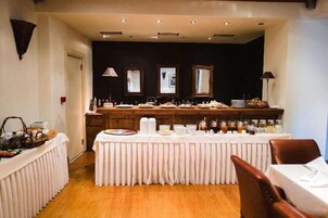 Montaje de bufé con una larga mesa cubierta por un mantel blanco, rodeada de sillas.