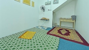 A small room with a checkered floor, a bed with a patterned bedspread, a fan, and a small table with a cushion. - D'pearl Hotel (George Town)