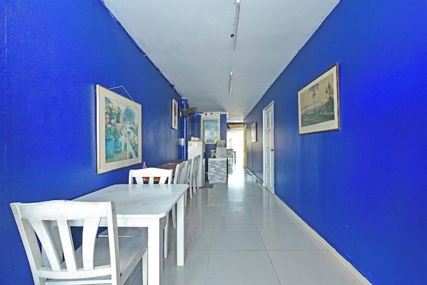A hallway with blue walls, white ceiling, and white floor tiles. There are framed pictures on the walls and a table with chairs at the end of the hallway. - D'pearl Hotel (George Town)