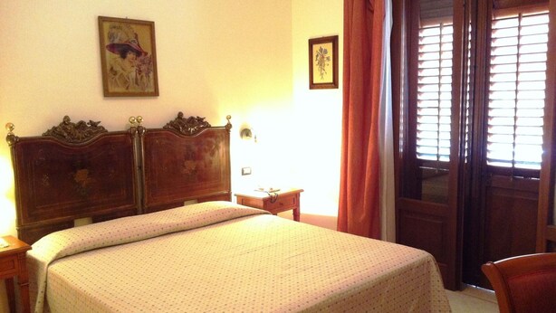 A neatly made bed with a wooden headboard, a small bedside table, and a wall-mounted light. - Hotel Mediterraneo (San Vito Lo Capo)