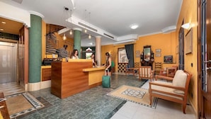 A hotel lobby with a reception desk, a staircase, and a seating area with a sofa and chairs. - Hotel Mediterraneo (San Vito Lo Capo)