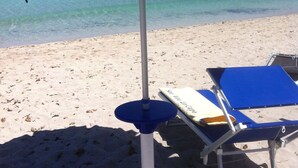 A beach with a blue umbrella and a lounge chair. - Hotel Mediterraneo (San Vito Lo Capo)
