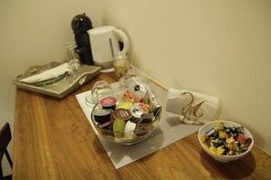 A wooden table with a glass container holding various food items, a white bowl with chocolates, and a coffee maker in the background. - B&B Chez Moi (Bologna)