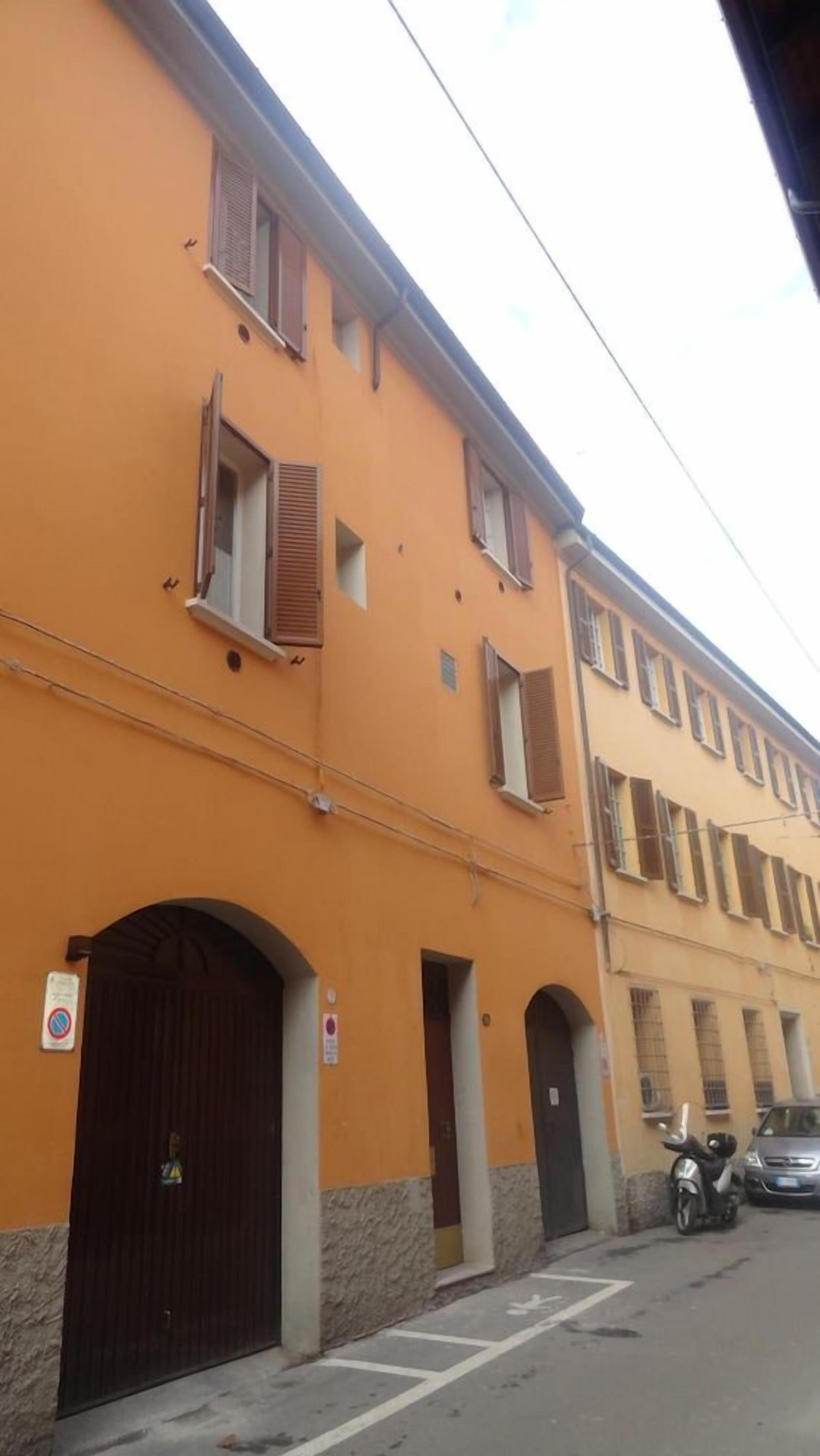 A multi-story building with a yellow facade, multiple windows with shutters, and a dark brown entrance door.