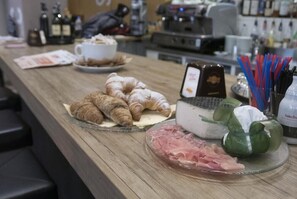 Un comptoir pour le petit-déjeuner avec des croissants, du fromage, du jambon et une machine à café.