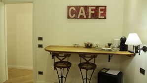A small kitchen area with a wooden counter, two bar stools, a coffee maker, a lamp, and a 'CAFE' sign on the wall. - B&B Chez Moi (Bologna)