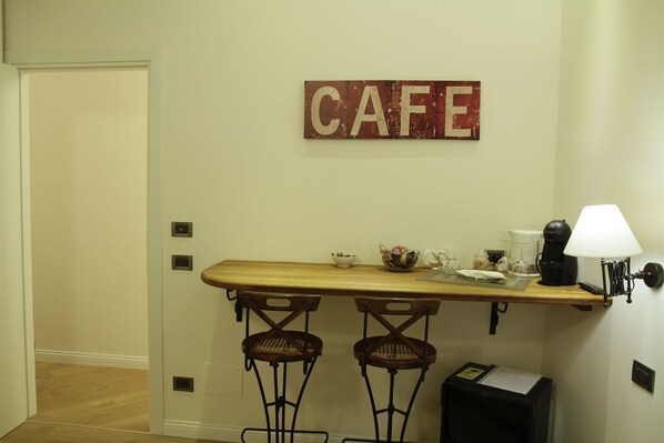 A small kitchen area with a wooden counter, two bar stools, a coffee maker, a lamp, and a 'CAFE' sign on the wall. - B&B Chez Moi (Bologna)