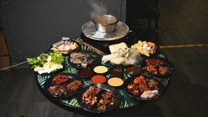 A table with various dishes and condiments, a hot pot on top, and a chair in the background. - Dreamscape Apartment at Golden Hill (Tanah Rata)