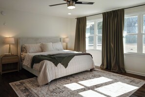 Quarto com cama, duas mesas de cabeceira, ventilador de teto e uma janela grande com cortinas.