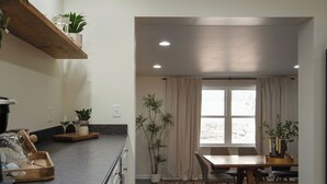 Una cocina moderna con encimera de madera, una zona de comedor con mesa y sillas, y una ventana con cortinas.