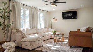 Una sala de estar moderna con un sofá modular, un sillón de cuero marrón, una mesa de centro y una lámpara de pie.