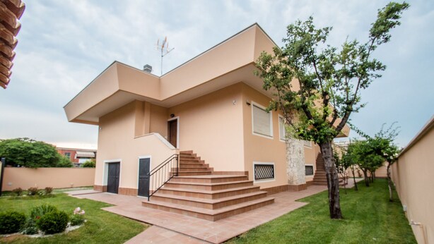 A modern two-story house with a flat roof, a central staircase, and a small garden area.