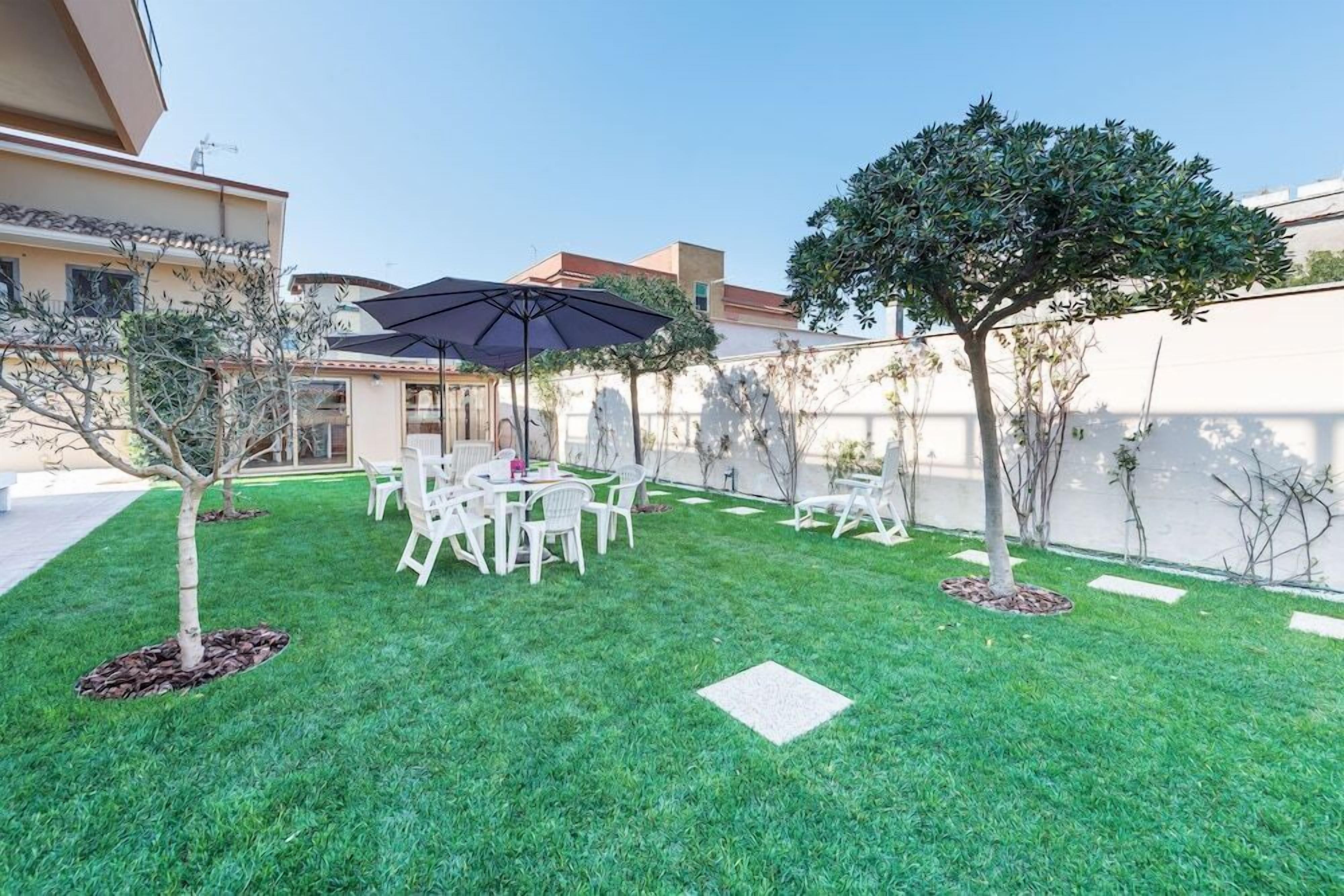 A well-maintained outdoor patio with a dining table and chairs, surrounded by a neatly trimmed lawn and small trees.