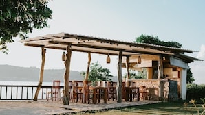 An outdoor dining area with wooden tables and chairs, a pergola, and a view of the water. - The Villa Dini Dnusa Lembongan (Lembongan Island)